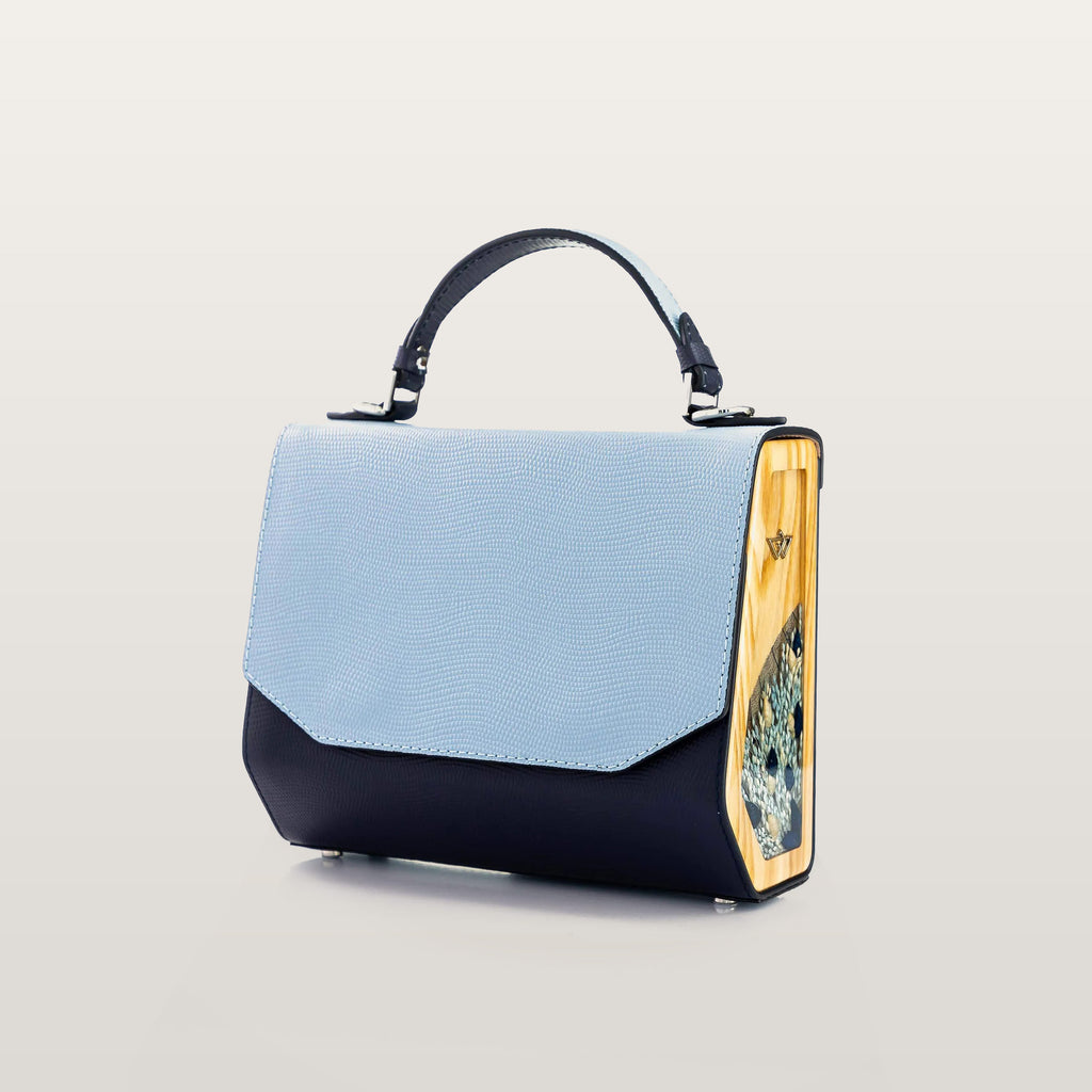 Handbag with a light blue top section and black bottom section on a beige background