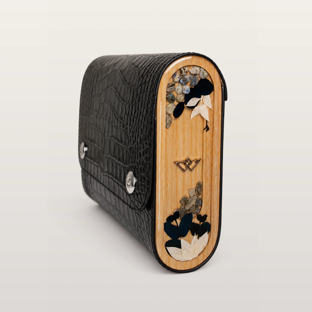 Black textured clutch with wooden side featuring floral designs on a light gray background