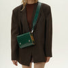 Person wearing a dark brown blazer with a green crocodile-patterned handbag.