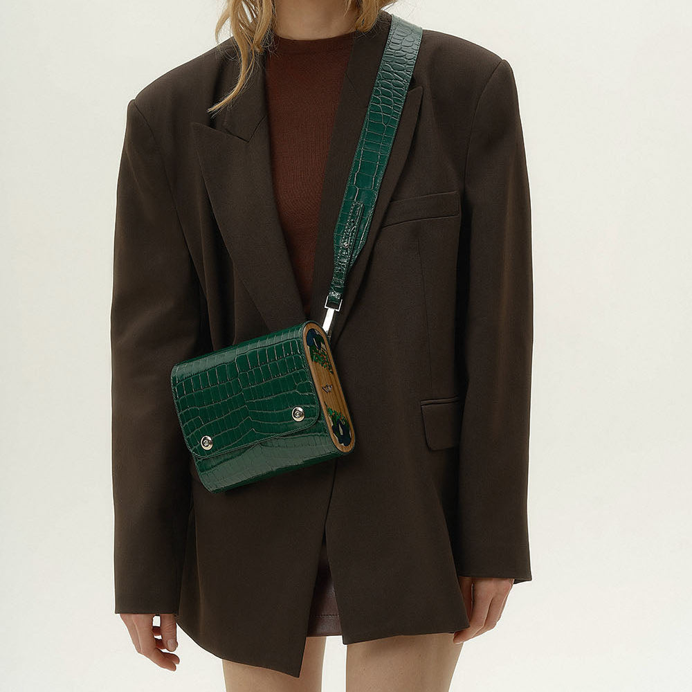 Person wearing a dark brown blazer with a green crocodile-patterned handbag.