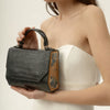 Woman holding a black textured handbag with a wooden accent against a neutral background